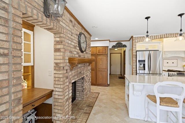 11781 W Herbison Rd, Eagle, MI 48822 - kitchen featuring appliances with stainless steel finishes, light countertops, decorative light fixtures, ornamental molding, and a brick fireplace