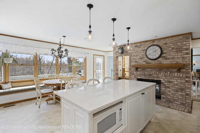 11781 W Herbison Rd, Eagle, MI 48822 - kitchen featuring white microwave, a fireplace, plenty of natural light, white cabinets, and crown molding