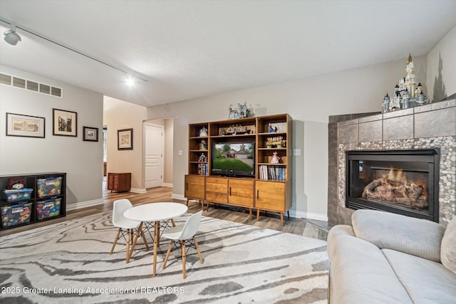 1058 Buckingham Rd, Haslett, MI 48840 - living room featuring rail lighting, wood finished floors, a fireplace, and baseboards