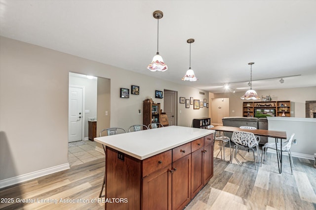 1058 Buckingham Rd, Haslett, MI 48840 - kitchen featuring light wood-type flooring, pendant lighting, a center island, light countertops, and baseboards