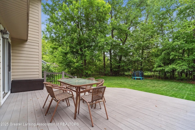1058 Buckingham Rd, Haslett, MI 48840 - wooden deck with a trampoline, a yard, outdoor dining space, and view of wooded area