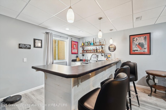 5619 Bittern Dr, Holt, MI 48842 - indoor wet bar with a paneled ceiling, light wood-style flooring, baseboards, and decorative light fixtures