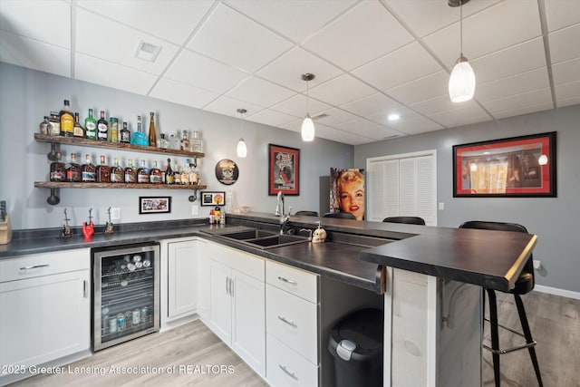 5619 Bittern Dr, Holt, MI 48842 - indoor wet bar featuring wine cooler, light wood-style flooring, a paneled ceiling, and hanging light fixtures