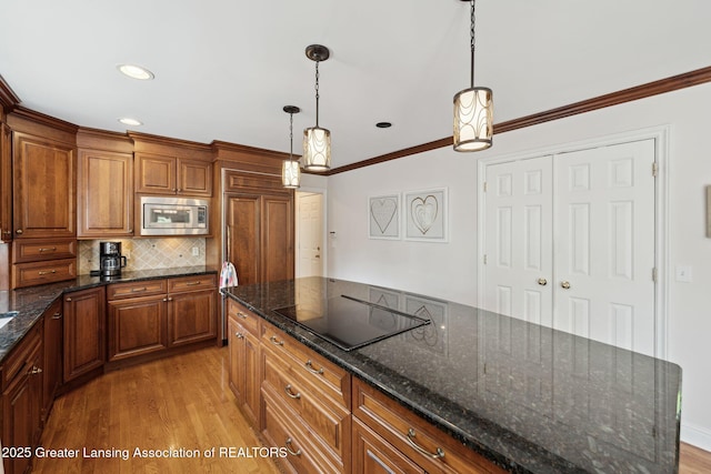 1209 Windale Pl, East Lansing, MI 48823 - kitchen with stainless steel microwave, black electric cooktop, light wood-type flooring, brown cabinetry, and backsplash