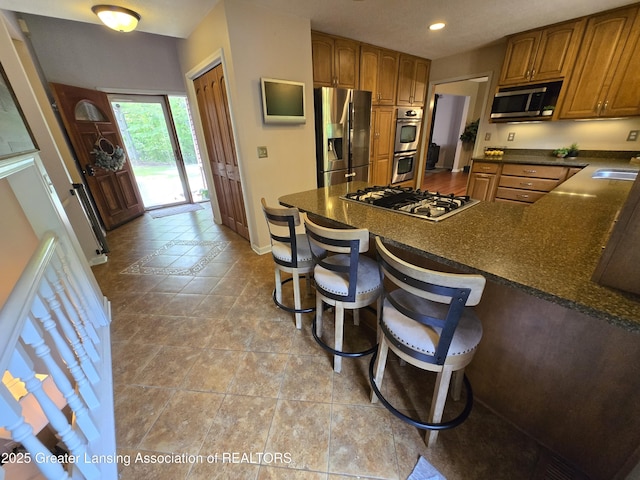 4423 Hyatt St, Eaton Rapids, MI 48827 - kitchen with stainless steel appliances, a peninsula, brown cabinetry, baseboards, and a breakfast bar