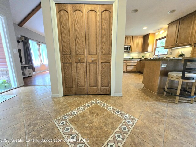 4423 Hyatt St, Eaton Rapids, MI 48827 - kitchen with stainless steel microwave, dark countertops, light tile patterned floors, brown cabinetry, and baseboards