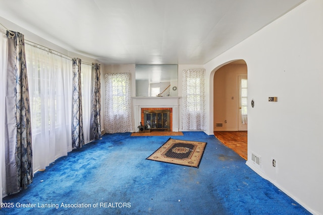 1615 Inverness Ave, Lansing, MI 48915 - unfurnished living room with arched walkways, carpet flooring, a brick fireplace, and baseboards