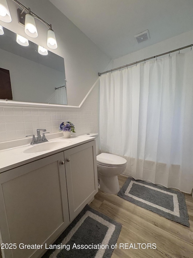 1524 Roseneath Ave, Lansing, MI 48915 - full bath with wood finished floors, vanity, toilet, tasteful backsplash, and tile walls