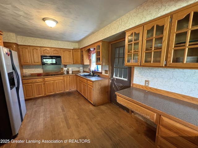 1064 W Shepherd St, Charlotte, MI 48813 - kitchen featuring black appliances, wallpapered walls, wood finished floors, brown cabinetry, and glass insert cabinets