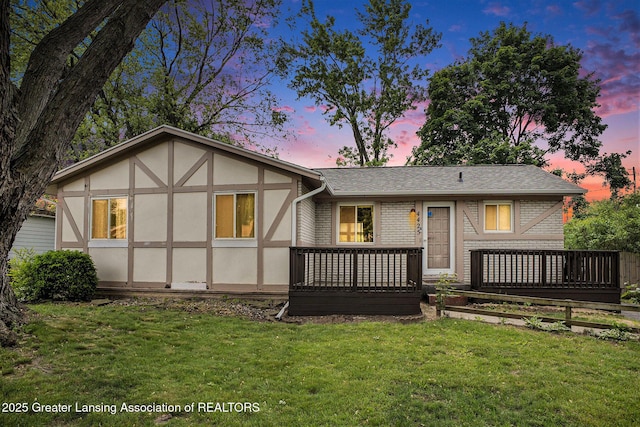 4425 Doncaster Ave, Holt, MI 48842 - back of house at dusk featuring a deck, a lawn, stucco siding, and brick siding
