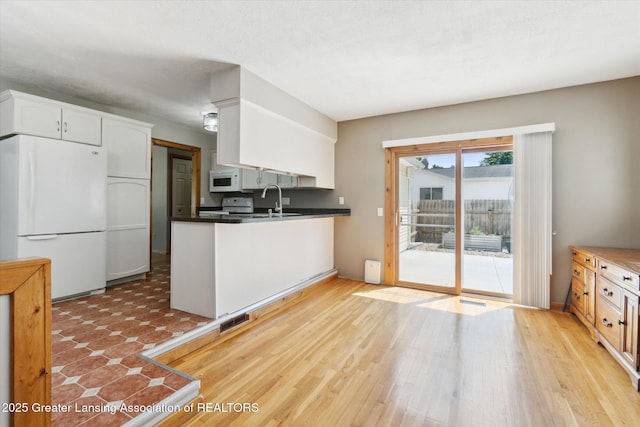 4663 Sycamore St, Holt, MI 48842 - kitchen with white appliances, white cabinetry, a peninsula, a sink, and dark countertops