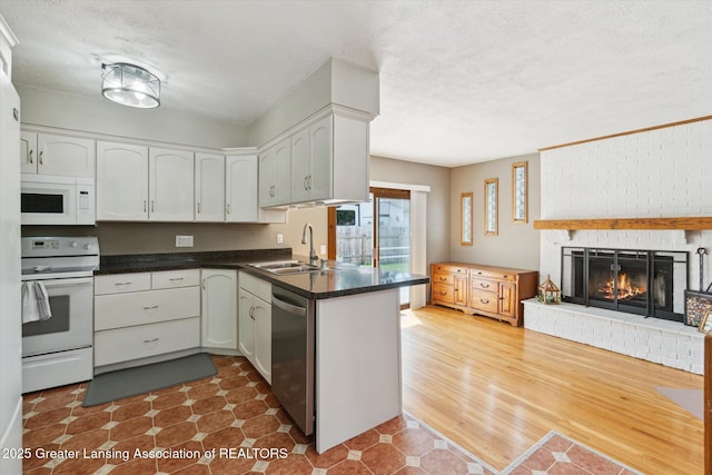 4663 Sycamore St, Holt, MI 48842 - kitchen featuring white appliances, a sink, dark countertops, a textured ceiling, and a brick fireplace