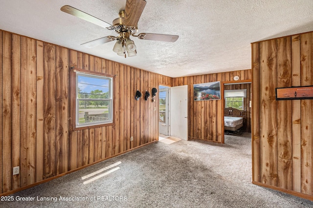 6327 Grovenburg Rd, Lansing, MI 48911 - empty room with plenty of natural light, a textured ceiling, wooden walls, ceiling fan, and carpet flooring