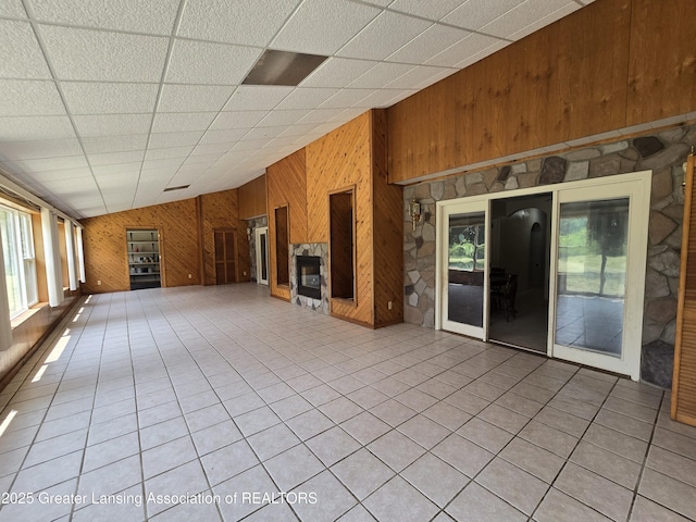 6322 Springport Rd, Eaton Rapids, MI 48827 - unfurnished living room with wood walls, healthy amount of natural light, a glass covered fireplace, light tile patterned floors, and a drop ceiling
