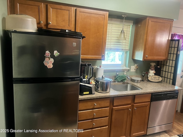 1745 Maisonette Dr, Lansing, MI 48911 - kitchen with stainless steel appliances, brown cabinets, a sink, light stone countertops, and pendant lighting