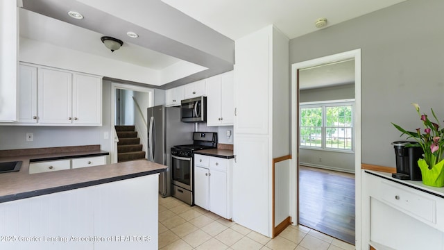 3326 W Willow St, Lansing, MI 48917 - kitchen featuring stainless steel appliances, dark countertops, white cabinets, light tile patterned floors, and baseboards