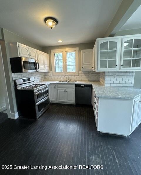 1141 N Genesee Dr, Lansing, MI 48915 - kitchen featuring appliances with stainless steel finishes, dark wood-style floors, glass insert cabinets, white cabinetry, and backsplash