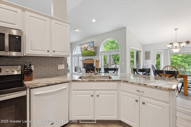 11782 Sara Ann Dr, Dewitt, MI 48820 - kitchen featuring stainless steel appliances, vaulted ceiling, a sink, decorative backsplash, and a fireplace