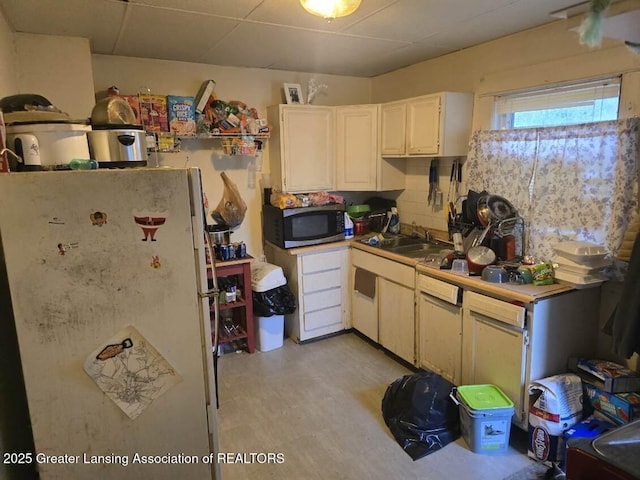 1417 Reo Ave, Lansing, MI 48910 - kitchen with freestanding refrigerator, stainless steel microwave, a sink, light floors, and white cabinets