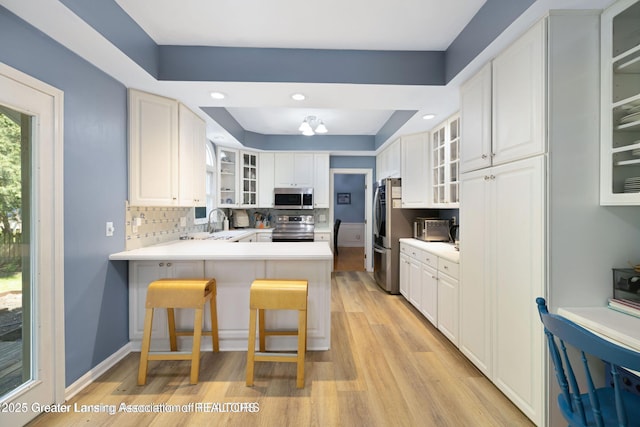 2038 Woodfield Rd, Okemos, MI 48864 - kitchen with stainless steel appliances, light wood-style floors, a peninsula, glass insert cabinets, and a raised ceiling