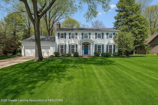 2038 Woodfield Rd, Okemos, MI 48864 - colonial house featuring a chimney, an attached garage, driveway, and a front yard