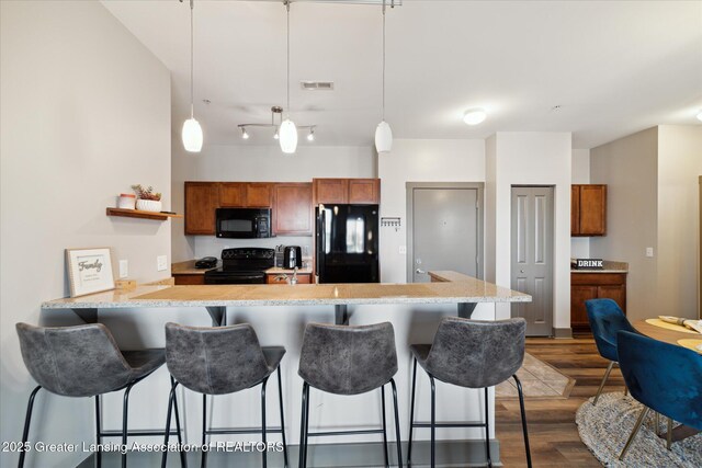 500 E Michigan Ave Unit 417, Lansing, MI 48912 - kitchen featuring black appliances, brown cabinetry, a peninsula, a breakfast bar, and dark wood-style floors