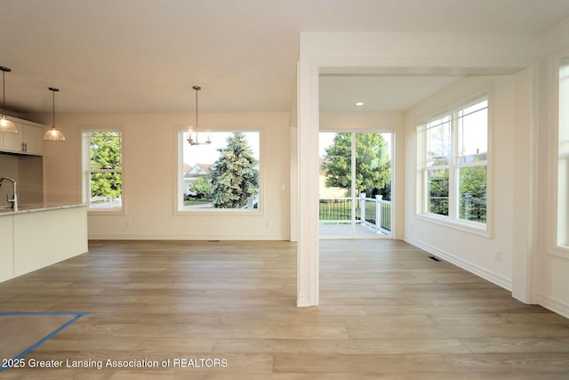 629 Aquila Dr, East Lansing, MI 48823 - unfurnished living room with plenty of natural light, light wood-type flooring, baseboards, and a chandelier