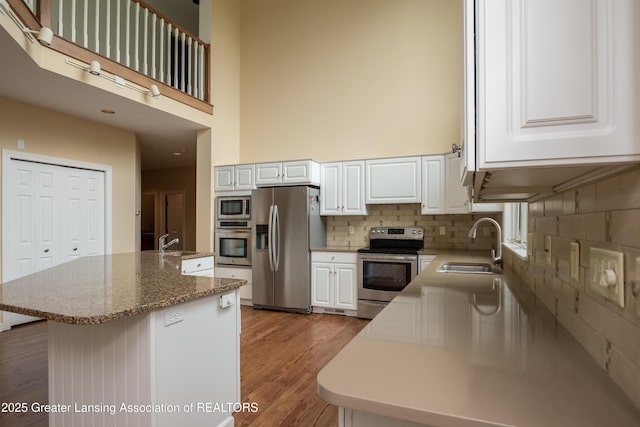 1120 Nautical Dr, Okemos, MI 48864 - kitchen with stainless steel appliances, light wood finished floors, a high ceiling, decorative backsplash, and white cabinets
