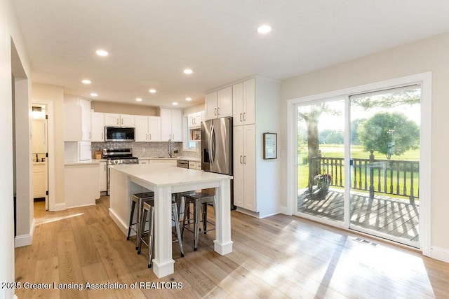 5871 Green Rd, Haslett, MI 48840 - kitchen with appliances with stainless steel finishes, light wood-style floors, white cabinets, light countertops, and decorative backsplash