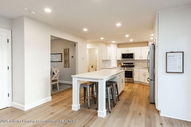 5871 Green Rd, Haslett, MI 48840 - kitchen with appliances with stainless steel finishes, a breakfast bar area, light wood-style floors, decorative backsplash, and white cabinetry