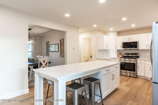 5871 Green Rd, Haslett, MI 48840 - kitchen with appliances with stainless steel finishes, white cabinetry, a breakfast bar, light wood-style flooring, and recessed lighting