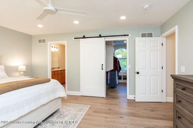 5871 Green Rd, Haslett, MI 48840 - bedroom featuring a walk in closet, a barn door, light wood finished floors, recessed lighting, and connected bathroom