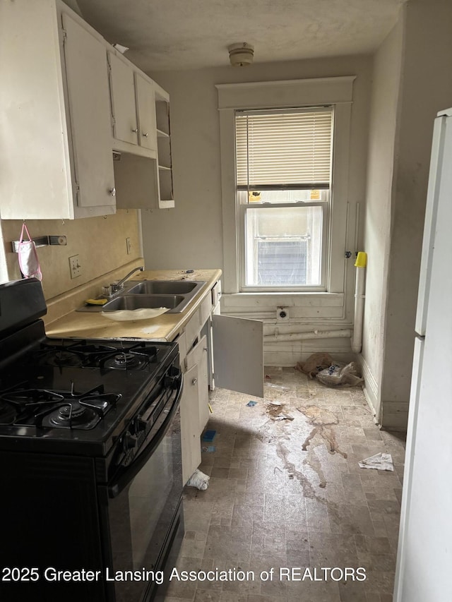 917 E Kalamazoo St, Lansing, MI 48912 - kitchen with black range with gas stovetop, a sink, freestanding refrigerator, white cabinets, and light countertops