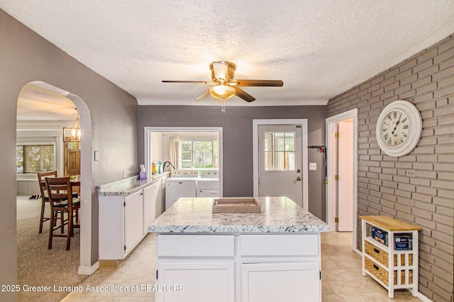 131 W S St, Williamston, MI 48895 - kitchen with ceiling fan, independent washer and dryer, arched walkways, white cabinetry, and brick wall