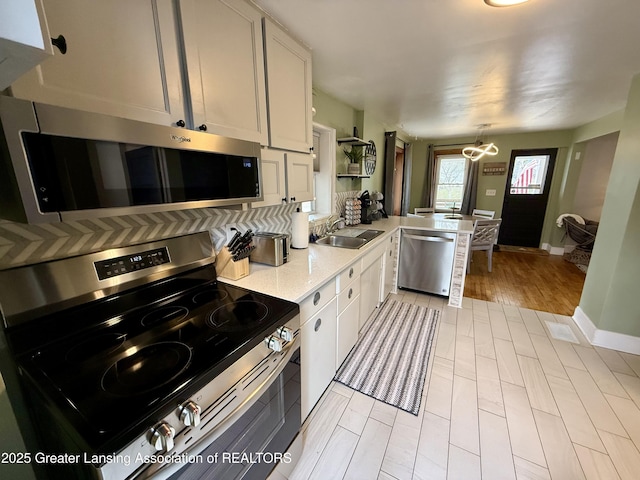 227 S Foster Ave, Lansing, MI 48912 - kitchen with stainless steel appliances, a sink, a peninsula, baseboards, and white cabinets