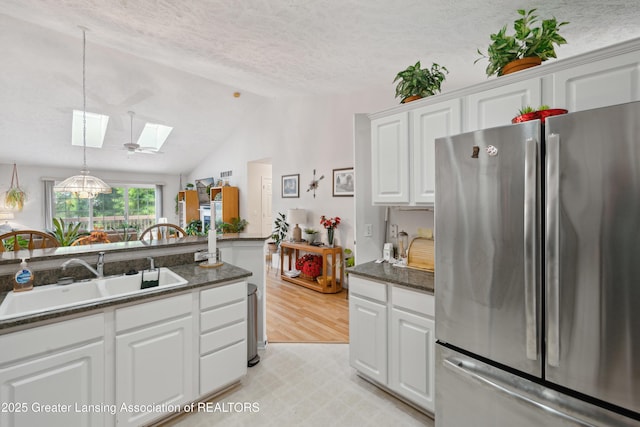 1703 Willow Creek Dr Unit 29, Lansing, MI 48917 - kitchen featuring freestanding refrigerator, a skylight, light floors, vaulted ceiling, and white cabinets