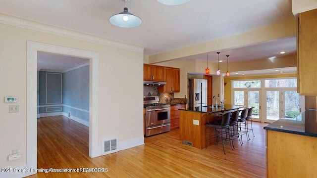 1046 Cresenwood Rd, East Lansing, MI 48823 - kitchen with appliances with stainless steel finishes, under cabinet range hood, light wood-type flooring, dark countertops, and a breakfast bar area