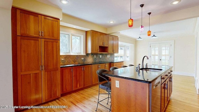 1046 Cresenwood Rd, East Lansing, MI 48823 - kitchen featuring light wood-type flooring, a kitchen breakfast bar, an island with sink, decorative backsplash, and brown cabinetry
