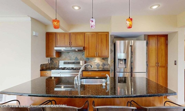 1046 Cresenwood Rd, East Lansing, MI 48823 - kitchen featuring stainless steel appliances, under cabinet range hood, brown cabinets, backsplash, and a center island with sink