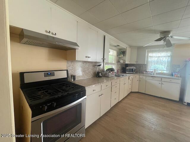 4022 Stabler St, Lansing, MI 48910 - kitchen with stainless steel appliances, ventilation hood, open shelves, light wood-style flooring, and white cabinetry