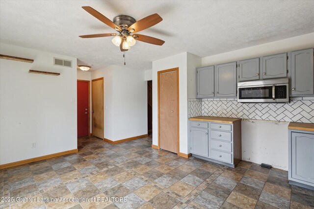 202 Kerry St, Eaton Rapids, MI 48827 - kitchen featuring stainless steel microwave, gray cabinetry, stone finish flooring, and backsplash