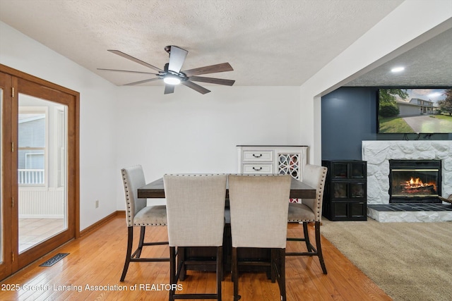 921 Ives Rd, Mason, MI 48854 - dining area with a textured ceiling, a ceiling fan, a stone fireplace, light wood finished floors, and baseboards
