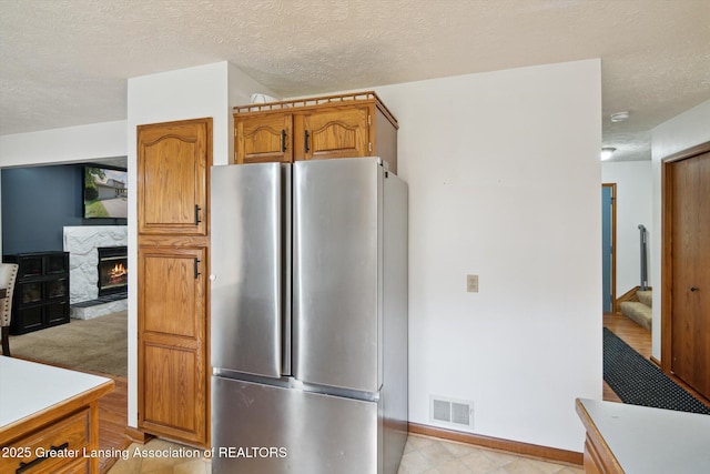 921 Ives Rd, Mason, MI 48854 - kitchen with freestanding refrigerator, brown cabinetry, light countertops, a textured ceiling, and a warm lit fireplace