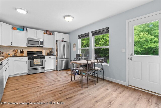 460 Blue Spruce Ln, Mason, MI 48854 - kitchen with stainless steel appliances, light wood-style floors, white cabinetry, and tasteful backsplash