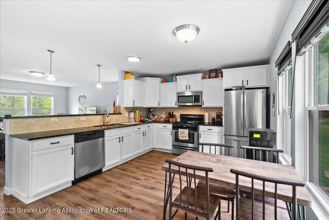 460 Blue Spruce Ln, Mason, MI 48854 - kitchen featuring appliances with stainless steel finishes, a peninsula, backsplash, white cabinetry, and wood finished floors
