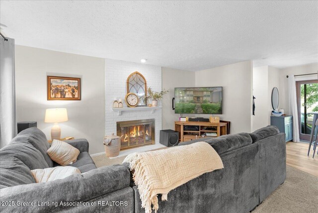 992 Touraine Ave, East Lansing, MI 48823 - living room featuring a textured ceiling, a brick fireplace, light wood-style flooring, and light carpet