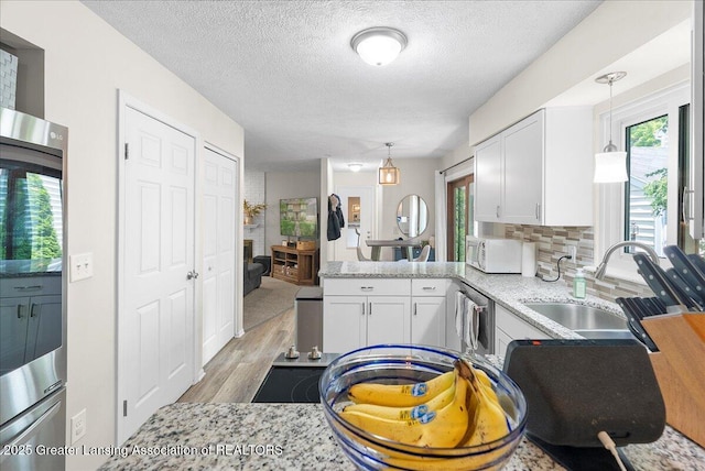 992 Touraine Ave, East Lansing, MI 48823 - kitchen with white microwave, a peninsula, a sink, white cabinetry, and a textured ceiling