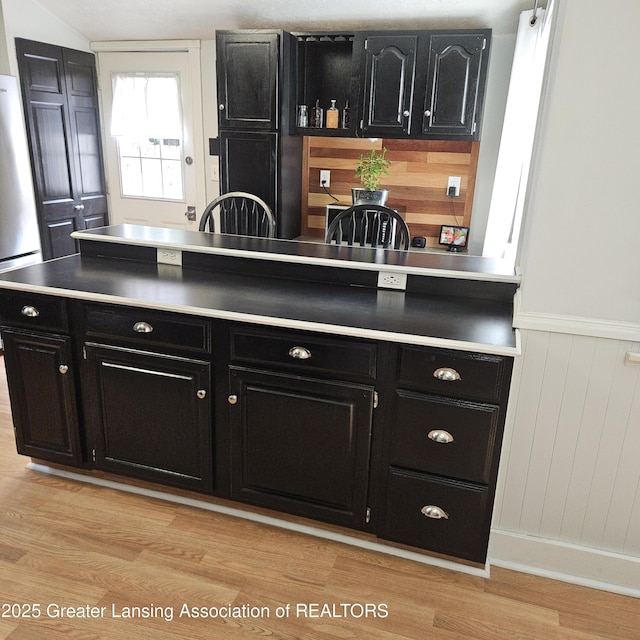 405 E Shaw St, Charlotte, MI 48813 - kitchen featuring dark cabinets, stainless steel refrigerator, light wood-style floors, and wainscoting