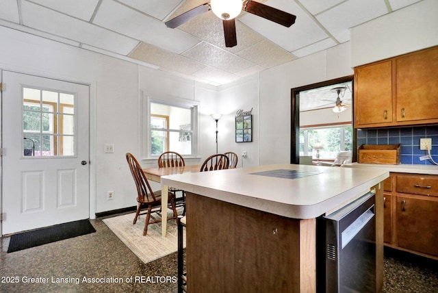 8767 Corrison Rd, Grand Ledge, MI 48837 - kitchen with a ceiling fan, dishwashing machine, brown cabinetry, a paneled ceiling, and backsplash