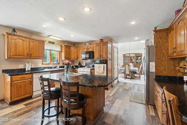 2020 Sunset Dr, Owosso, MI 48867 - kitchen featuring white appliances, wood finished floors, a center island with sink, brown cabinetry, and a breakfast bar area